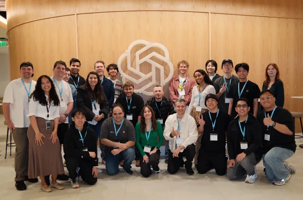 Community members posing together in front of an OpenAI logo on a wooden wall